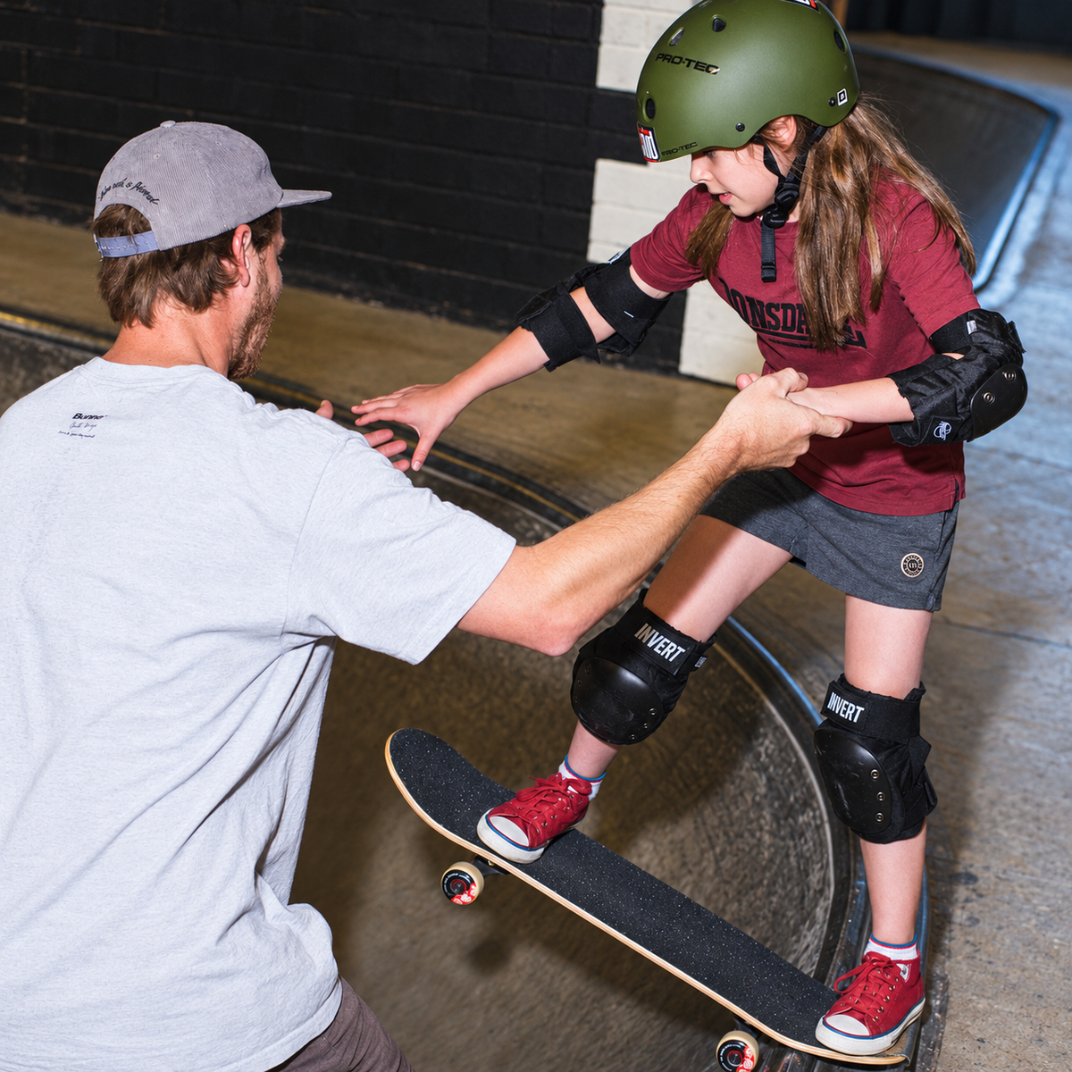 Beyond Skate coach helping a helmeted young skater balance on a skateboard during a clinic